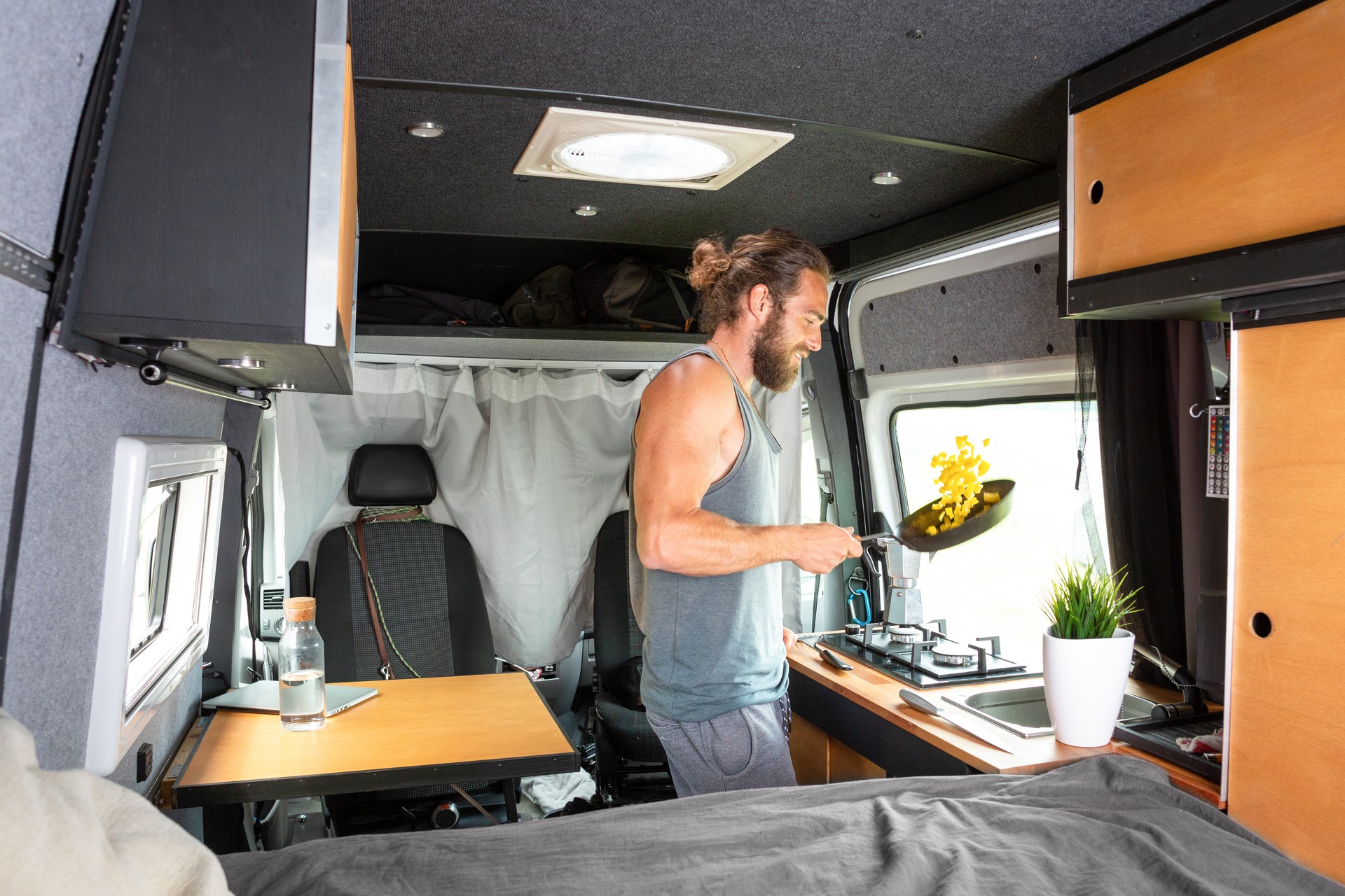 Man inside a camper van is cooking on a gas stove